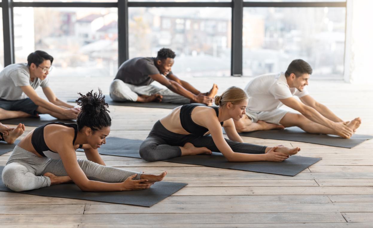 Cours de yoga collectif avec des hommes et des femmes réalisant des mouvements d’étirement sur le sol. 